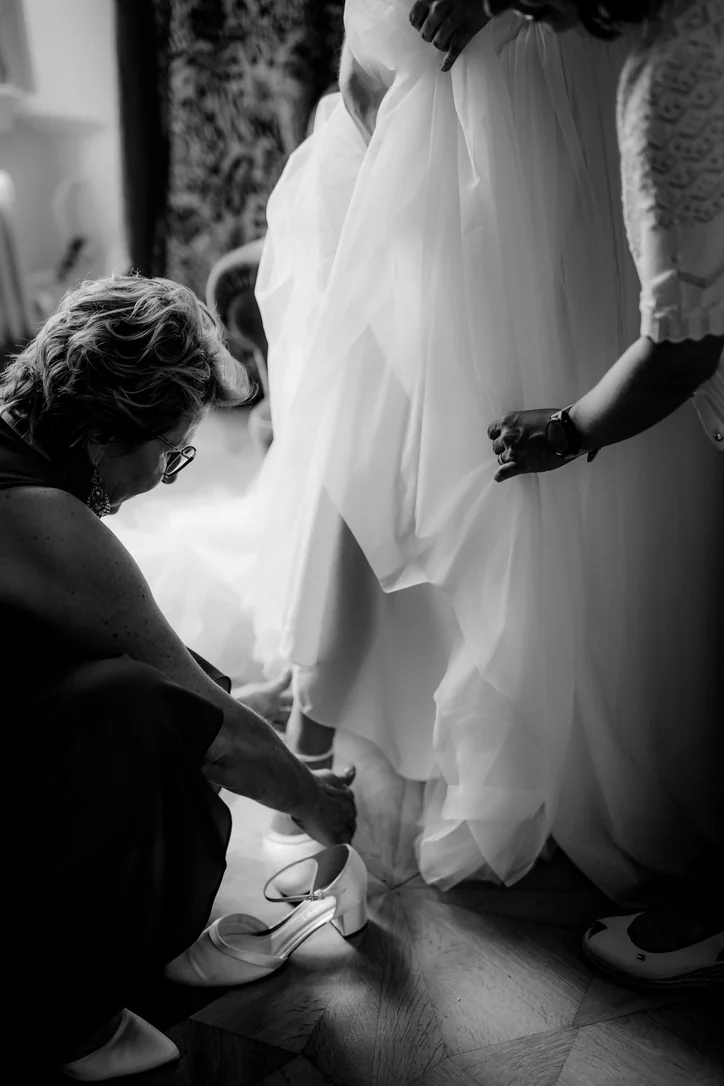 Schwarzweißaufnahme beim Anziehen der Brautschuhe vor der familiären Hochzeit im Schloss